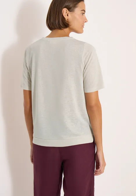 Vrouw van achteren in licht T-shirt en bordeauxrode broek voor een neutrale achtergrond.