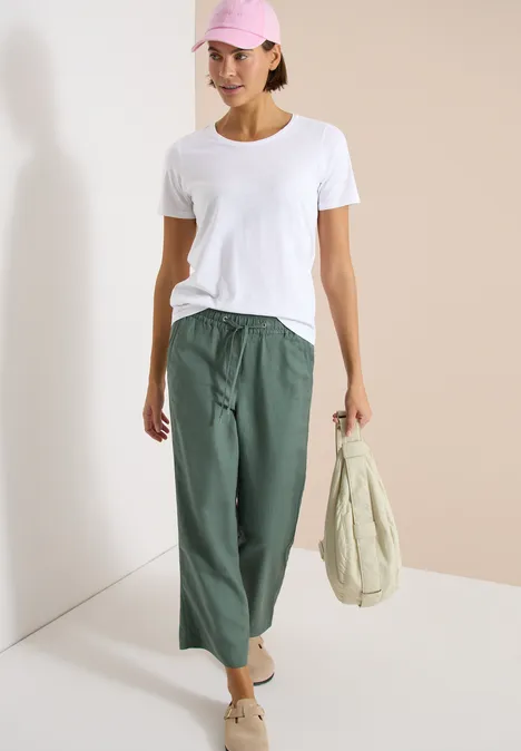 Basic T-Shirt mit Rundhals im 2er-Pack urban taupe/white Modell trägt weißes T-Shirt, olivgrüne, weite Hose und bequeme Schuhe und hält eine beige Tasche vor hellem Hintergrund.