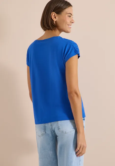 Kurzarm Shirt mit Boatneck und Raffung surf blue Frau von hinten in blauem T-Shirt und hellen Jeans vor schlichtem, beigem Hintergrund.