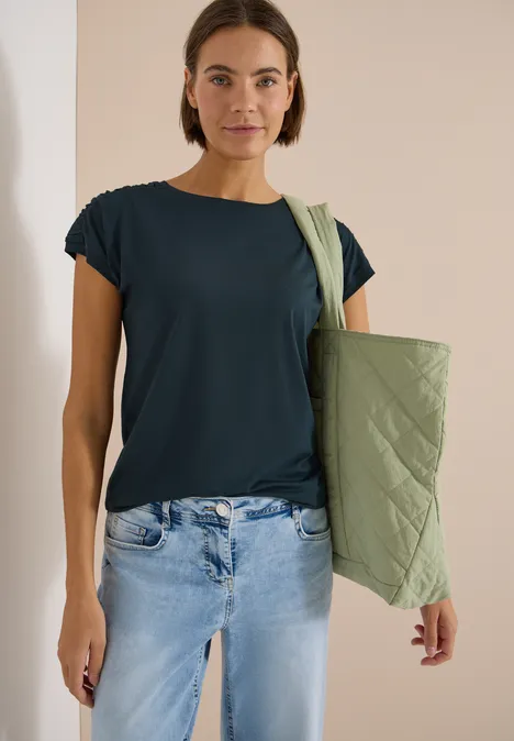 Kurzarm Shirt mit Boatneck und Raffung deep petrol blue Frau in dunkelblauem T-Shirt, hellen Jeans und grüner Stepp-Umhängetasche.