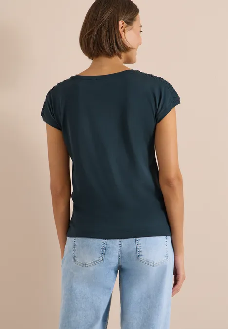 Kurzarm Shirt mit Boatneck und Raffung deep petrol blue Eine Frau steht mit dem Rücken zur Kamera, trägt ein dunkelgrünes T-Shirt und hellblaue Jeans.