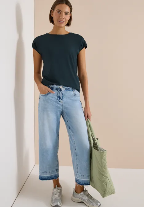 Kurzarm Shirt mit Boatneck und Raffung deep petrol blue Person trägt schwarzes T-Shirt, weite helle Jeans und hält eine große grüne Stofftasche.