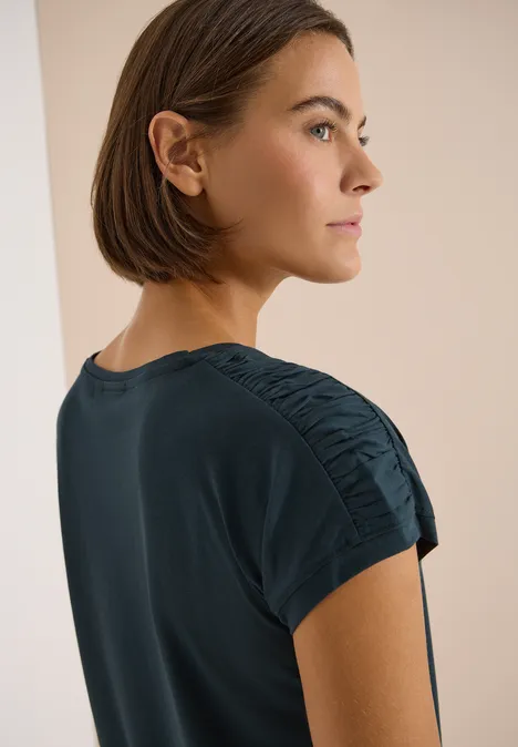 Kurzarm Shirt mit Boatneck und Raffung deep petrol blue Frau im Profil mit mittellangem Bob und dunkelblauem, gerafftem T-Shirt-Ärmel vor neutralem Hintergrund.