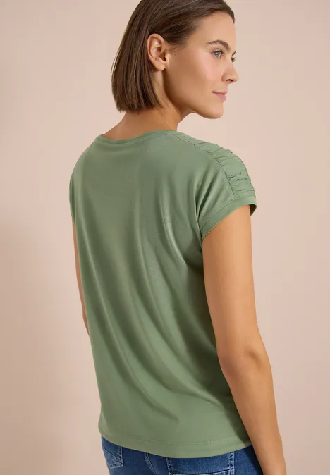 Kurzarm Shirt mit Boatneck und Raffung deep matcha green Frau von hinten in grünem T-Shirt mit gerafften Ärmeln und Jeans vor beigem Hintergrund.