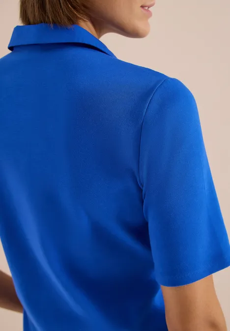 Eine Frau mit blauem Kurzarmshirt, Rücken und Teil des Gesichts sind sichtbar.
