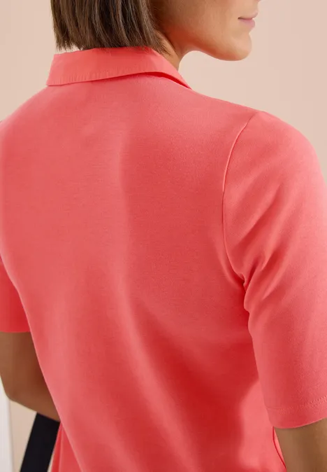Rückansicht einer Frau, die ein korallenfarbenes Poloshirt trägt.