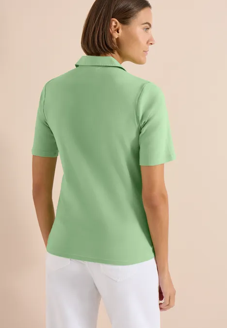 Basic Poloshirt mit Kurzarm juicy lime Rückenansicht einer Frau in hellgrünem Poloshirt und weißen Hosen vor hellem, neutralem Hintergrund.