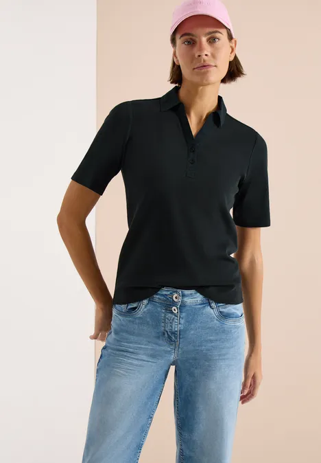 Basic Poloshirt mit Kurzarm palm breeze green Frau in schwarzem Polohemd und blauen Jeans steht vor hellem Hintergrund.