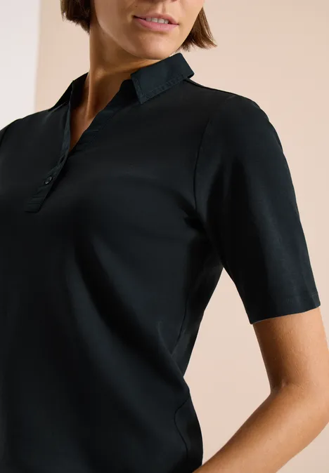 Basic Poloshirt mit Kurzarm palm breeze green Eine Frau trägt ein schwarzes, kurzärmeliges Poloshirt mit Stehkragen.