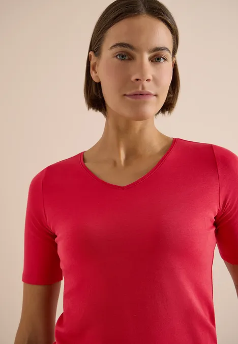 Frau mit rotem V-Ausschnittshirt und verschwommenem Gesicht vor beigem Hintergrund.