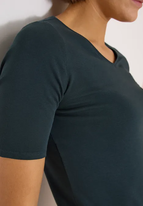 Seitliche Nahaufnahme einer Frau in einem dunkelgrünen, kurzärmligen V-Ausschnitt-Shirt.