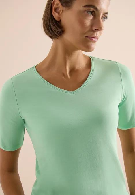 Eine Person trägt ein hellgrünes, kurzärmeliges V-Ausschnittshirt vor hellem Hintergrund.