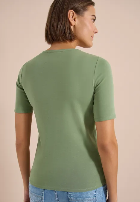 Basic T-Shirt aus Baumwolle deep matcha green Frau von hinten in grünem Kurzarmshirt und Jeans vor hellem Hintergrund.