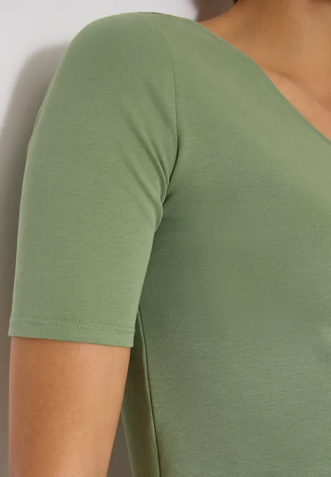 Basic T-Shirt aus Baumwolle deep matcha green Seitliche Ansicht einer Person mit engem kurzärmligem, grünen Oberteil vor weißem Hintergrund.