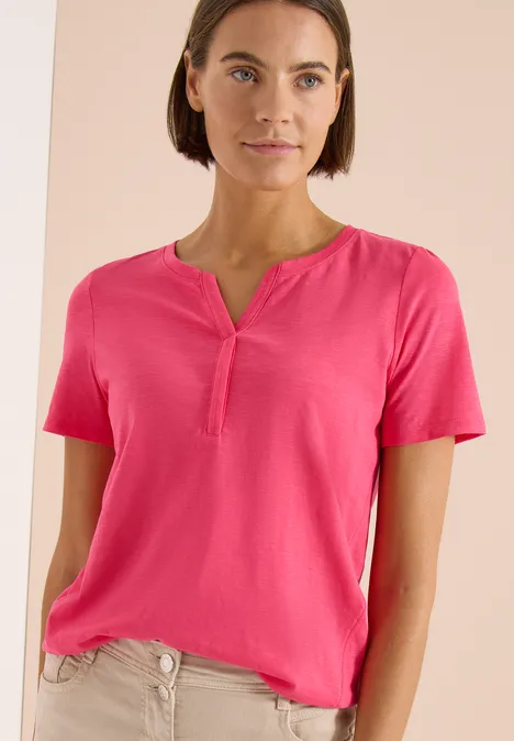 Frau in pinkem Kurzarmshirt vor neutralem Hintergrund.