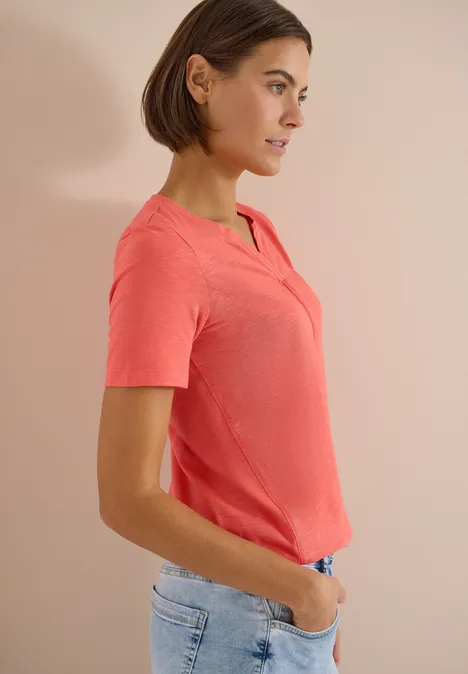 Basic Shirt im Tunika-Look shiny coral Frau in rosa T-Shirt und Jeans, seitlich, Hände in den Taschen.
