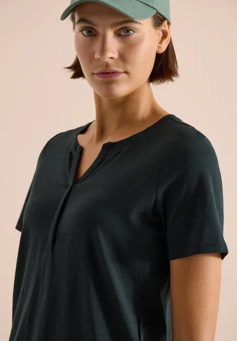 Persoon draagt een donkerblauw T-shirt met korte mouwen en Henley-hals, en een groene pet.