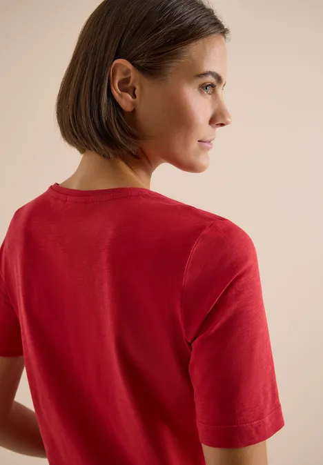 Eine Person von hinten in einem roten T-Shirt vor neutralem Hintergrund.