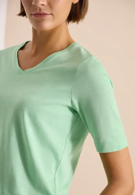 Frau in mintgrünem V-Ausschnitt-T-Shirt vor neutralem Hintergrund.