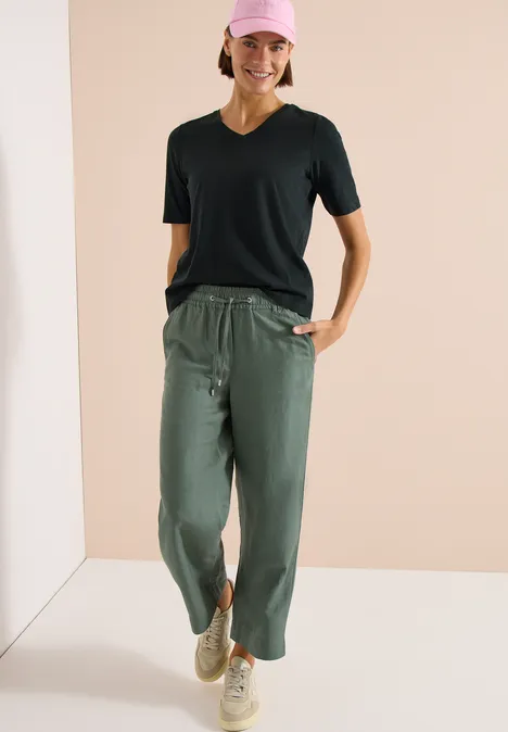 Frau in schwarzem T-Shirt, legerer olivgrüner Hose mit Tunnelzug und beigen Sneakern.