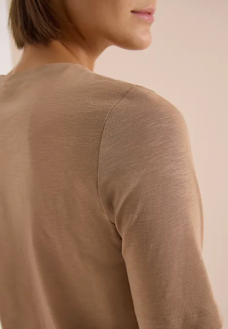 Basic T-Shirt mit Kurzarm und V-Neck creamy mocha Frau im beigen Langarmshirt, von hinten fotografiert, der Kopf leicht nach rechts gedreht.