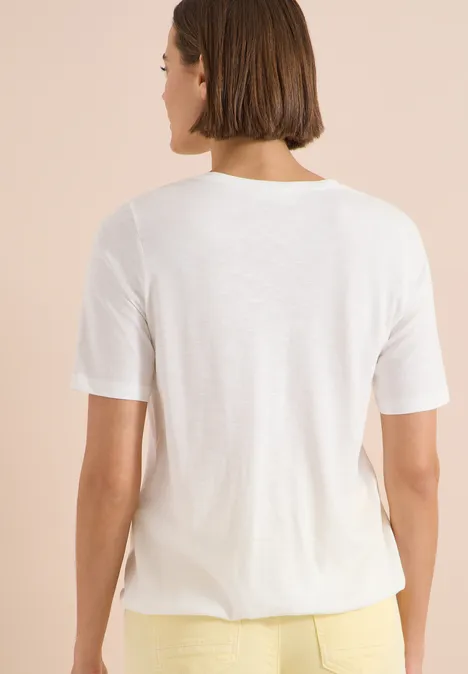 Vrouw van achteren in een eenvoudig wit T-shirt en gele broek voor een neutrale achtergrond.