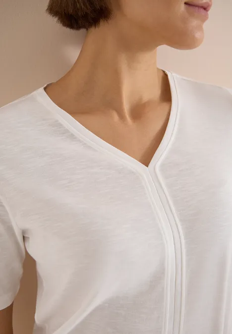 Een vrouw draagt een wit T-shirt met V-hals, te zien van hals tot borst.