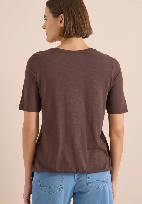 Kurzarm T-Shirt im Tunika-Look brown cacao Frau steht mit dem Rücken zur Kamera, trägt ein braunes T-Shirt und hellblaue Jeans, schulterlanges Haar.