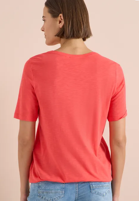 Personne de dos, portant un t-shirt rouge et un jean devant un fond uni clair.