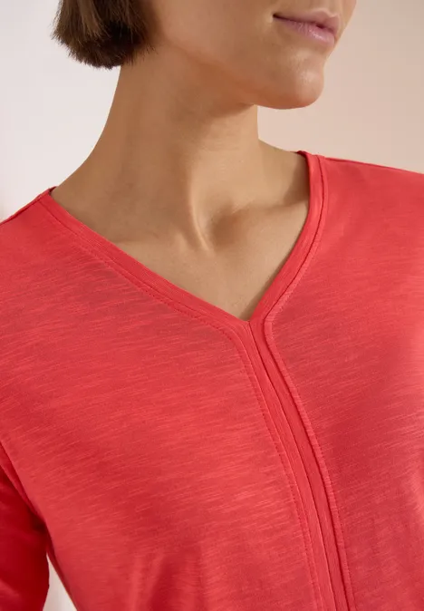 Femme portant un haut rouge à encolure en V, accent sur le cou et l'épaule
