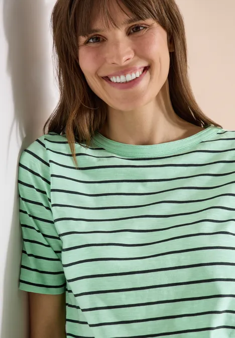 Person in mintgrün-schwarz gestreiftem T-Shirt lehnt an Wand, Gesicht unscharf