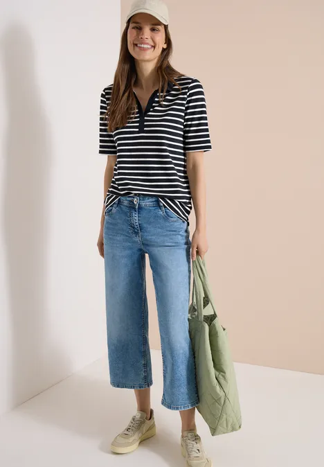 Frau trägt gestreiftes Poloshirt, weite Cropped-Jeans, grüne Sneaker und eine grüne Stofftasche.
