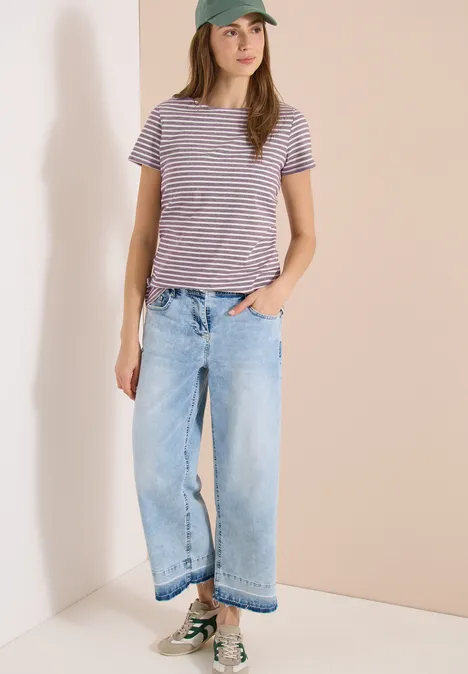 Persoon met gestreept T-shirt, wijde jeans en sneakers staat in een lichte hoek.