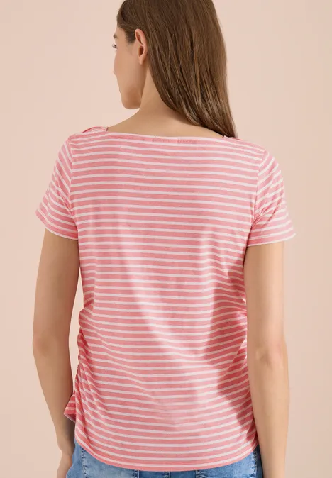 Koszulka w paski shiny coral Widok z tyłu kobiety w różowo-białym paskowanym t-shircie na jasnym tle.