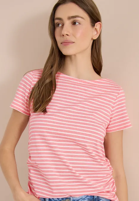 Koszulka w paski shiny coral Młoda kobieta ma na sobie różowo-biały, w paski t-shirt z krótkim rękawem na neutralnym tle.