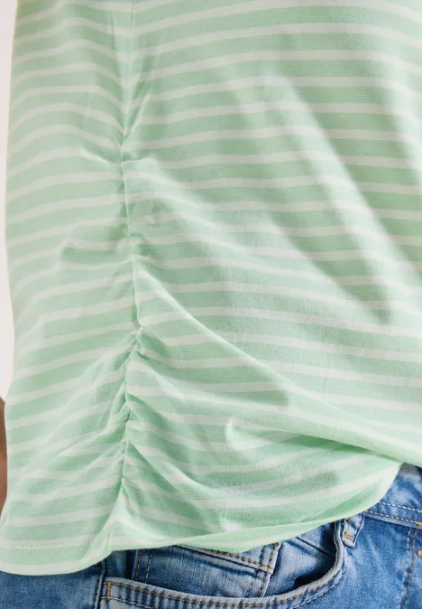 T-shirt rayé vert clair et blanc avec fronces latérales, porté avec un jean bleu.