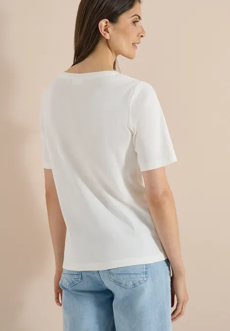 Basic geribd Shirt vanilla white Vrouw van achteren in een wit T-shirt en lichtblauwe jeans voor een beige achtergrond.