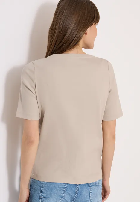 Frau von hinten in beigefarbenem T-Shirt und blauen Jeans.