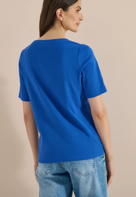 Basic Shirt met geribde textuur surf blue Een persoon heeft de rug naar de camera gekeerd, draagt een koningsblauw T-shirt en blauwe spijkerbroek.