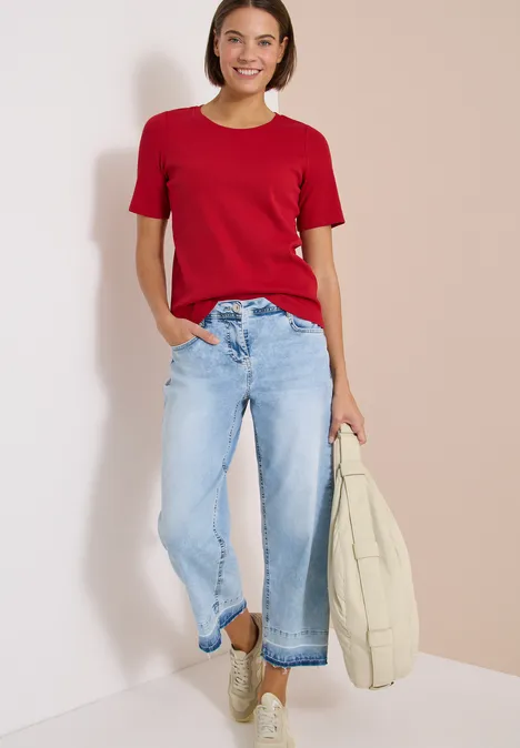 Basic T-Shirt in Rippstruktur tamarillo red Frau in rotem T-Shirt und hellblauen Jeans hält Tasche.