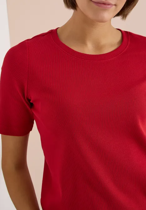 Basic T-Shirt in Rippstruktur tamarillo red Frau trägt rotes T-Shirt mit Rundhalsausschnitt, kurzärmlig, vor hellem Hintergrund.