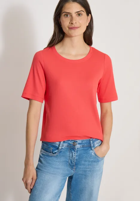 Basic Shirt met geribde textuur coral Vrouw in rood T-shirt en blauwe jeans voor neutrale achtergrond.