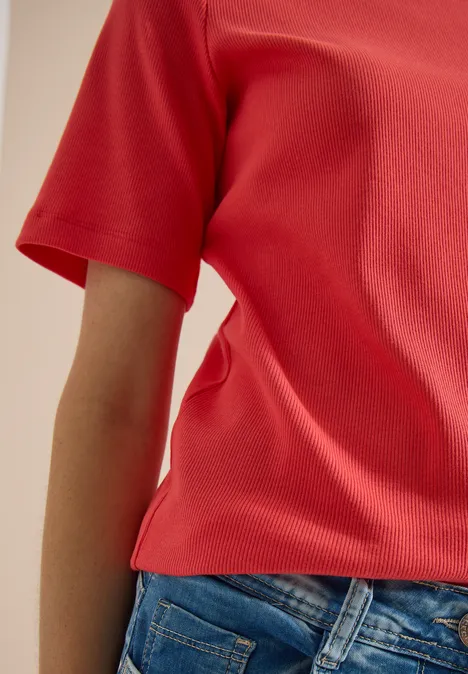 Basic Shirt met geribde textuur coral Een persoon draagt een rood shirt en blauwe jeans, gedeeltelijke weergave van het bovenlichaam