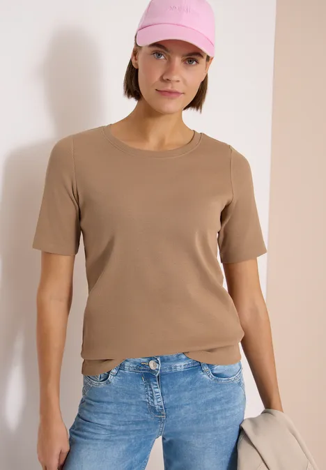 Persoon in lichtbruin T-shirt, blauwe jeans en roze pet met een lichte tas in de hand.