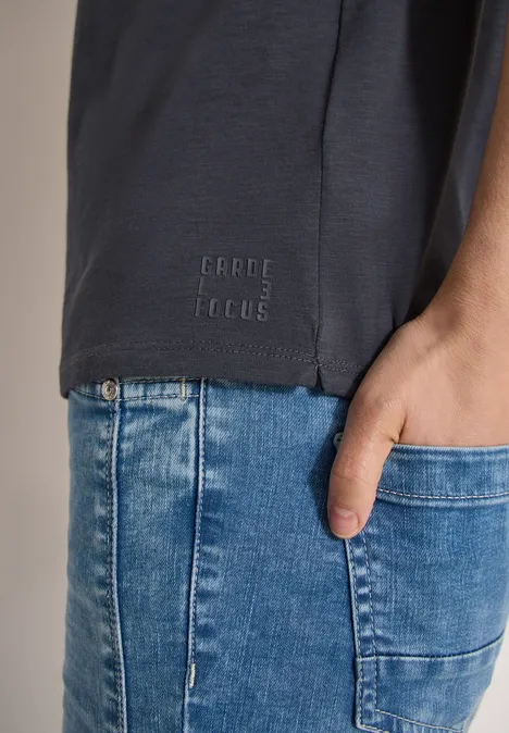 Torso mit dunkelgrauem T-Shirt und aufgedrucktem Logo, Hand in der vorderen Tasche blauer Jeans.