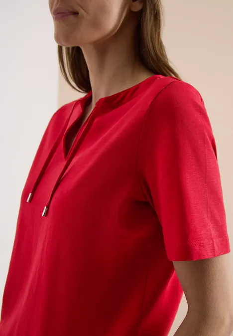 Frau trägt ein rotes, kurzärmeliges Oberteil mit V-Ausschnitt und Kordelzug-Details.