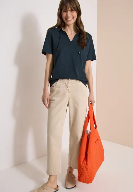 Frau trägt kurzärmliges dunkelblaues Hemd, beigefarbene Hose, beige Schuhe und orangefarbene Tasche