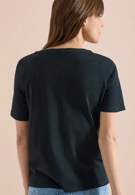 Frau von hinten in schlichtem schwarzem T-Shirt vor hellem Hintergrund.