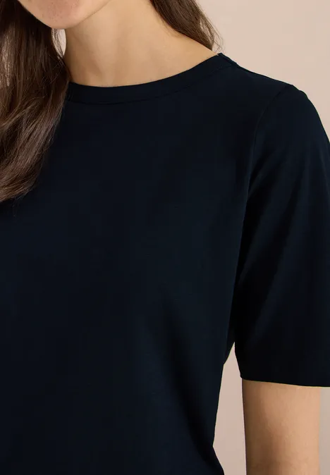 Vrouwelijk bovenlijf in een zwart T-shirt met korte mouwen, licht glimlachend.