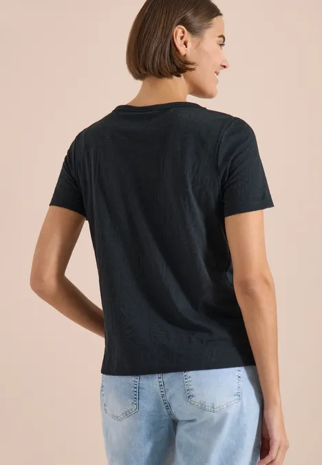 Kurzarm Shirt im Ausbrenner-Look palm breeze green Person in schwarzem T-Shirt und hellen Jeans von hinten vor beigem Hintergrund.